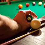 A vibrant, slightly hazy image inside a Spanish "bar" (bar de tapas). The focus is on a close-up of a billiards table, showcasing a player's hands carefully chalking a cue. Soft, warm light highlights the green felt and the polished cue ball. In the background, slightly out of focus, are patrons enjoying "tapas" and drinks, creating a lively yet relaxed atmosphere. The scene evokes the passion and community of billiards in a casual setting.